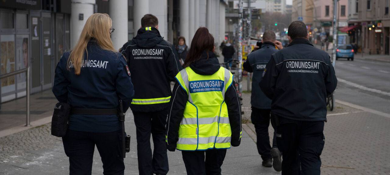 Städtische Mitarbeiter werden von Sicherheitskräften zu einem Termin begleitet.