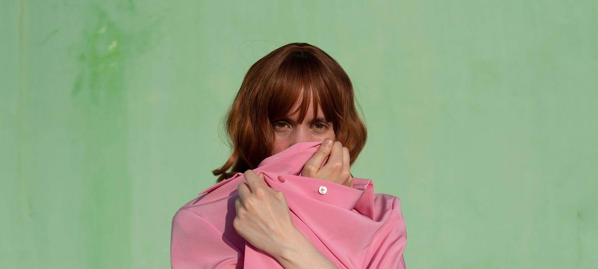 Eine Frau verdeckt ihr Gesicht mit einem pinkfarbenen Shirt