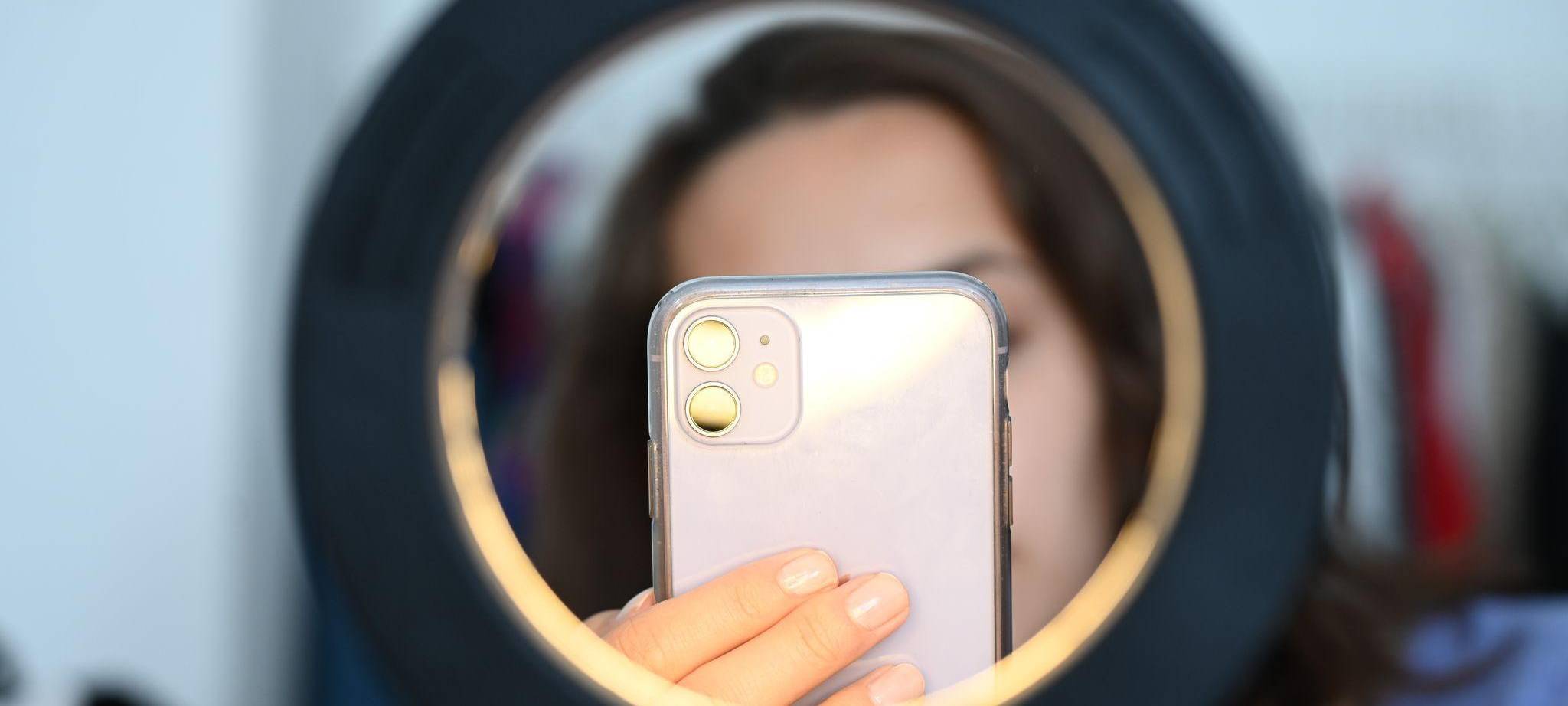 Influencer sitzt mit dem Smartphone hinter einem Ringlicht