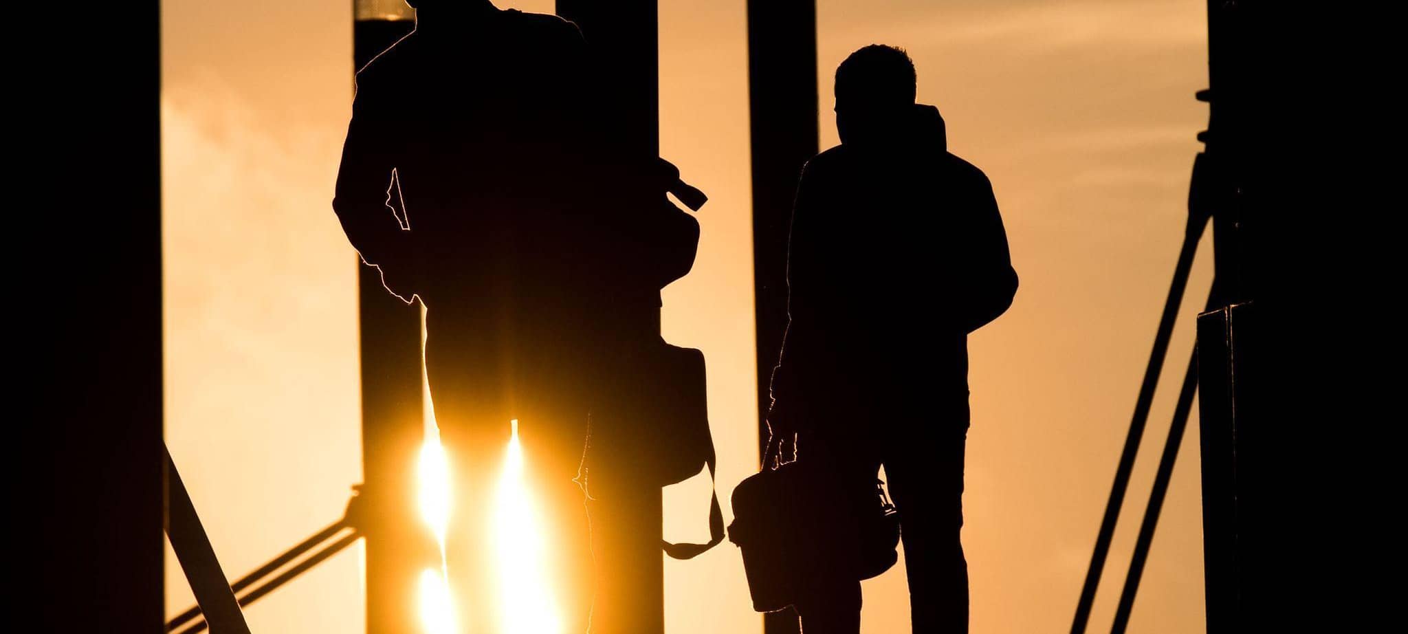Zwei Männer gehen mit Aktentasche bei Sonnenaufgang über Brücke